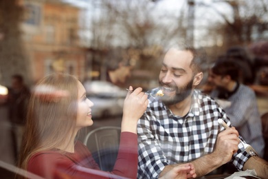 Photo of Lovely young couple spending time together in cafe, view from outdoors through window