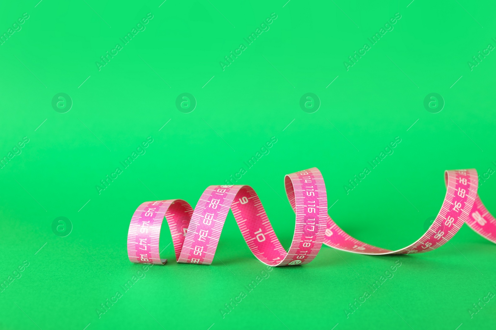 Photo of Pink measuring tape on green background, closeup