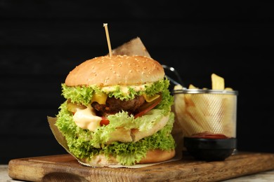 Photo of Burger with delicious patty, french fries and sauce on table against dark background