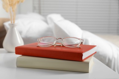 Photo of Books and glasses on white wooden bedside table in bedroom