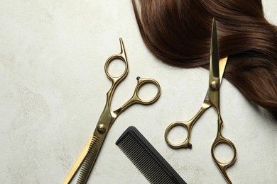 Photo of Professional hairdresser scissors and comb with brown hair strand on grey table, flat lay