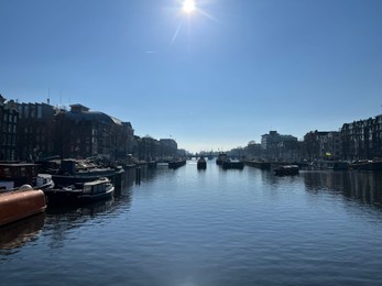 Photo of Amsterdam, Netherlands - March 01, 2023: Picturesque view of river embankment with moored boats in city under blue sky