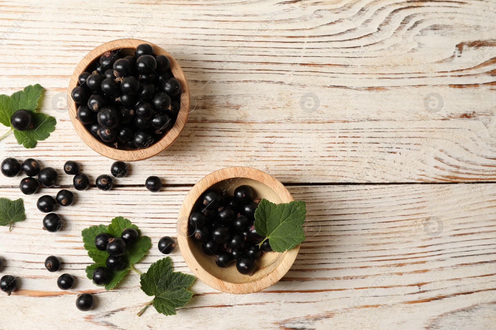 Photo of Ripe blackcurrants and leaves on light wooden table, flat lay. Space for text