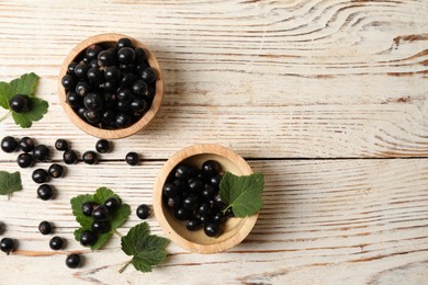 Photo of Ripe blackcurrants and leaves on light wooden table, flat lay. Space for text