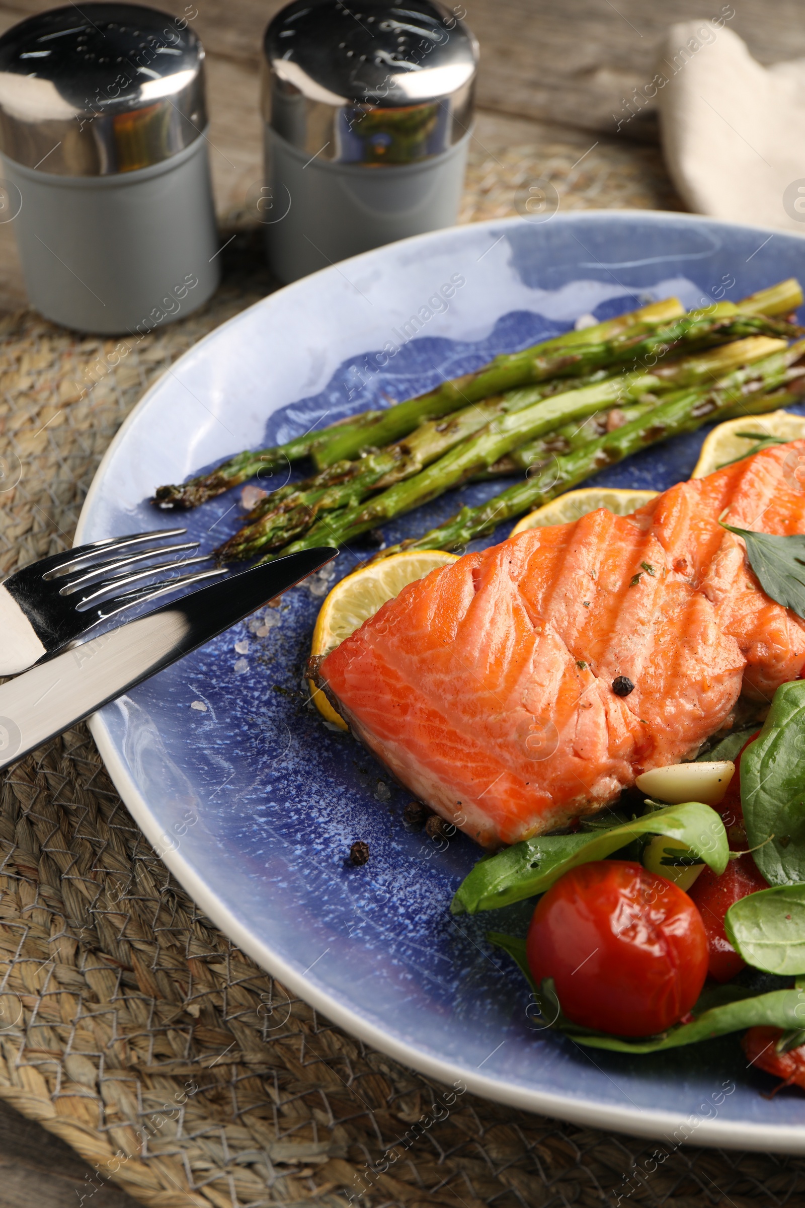 Photo of Tasty grilled salmon with tomatoes, asparagus, spinach and lemon served on table, closeup