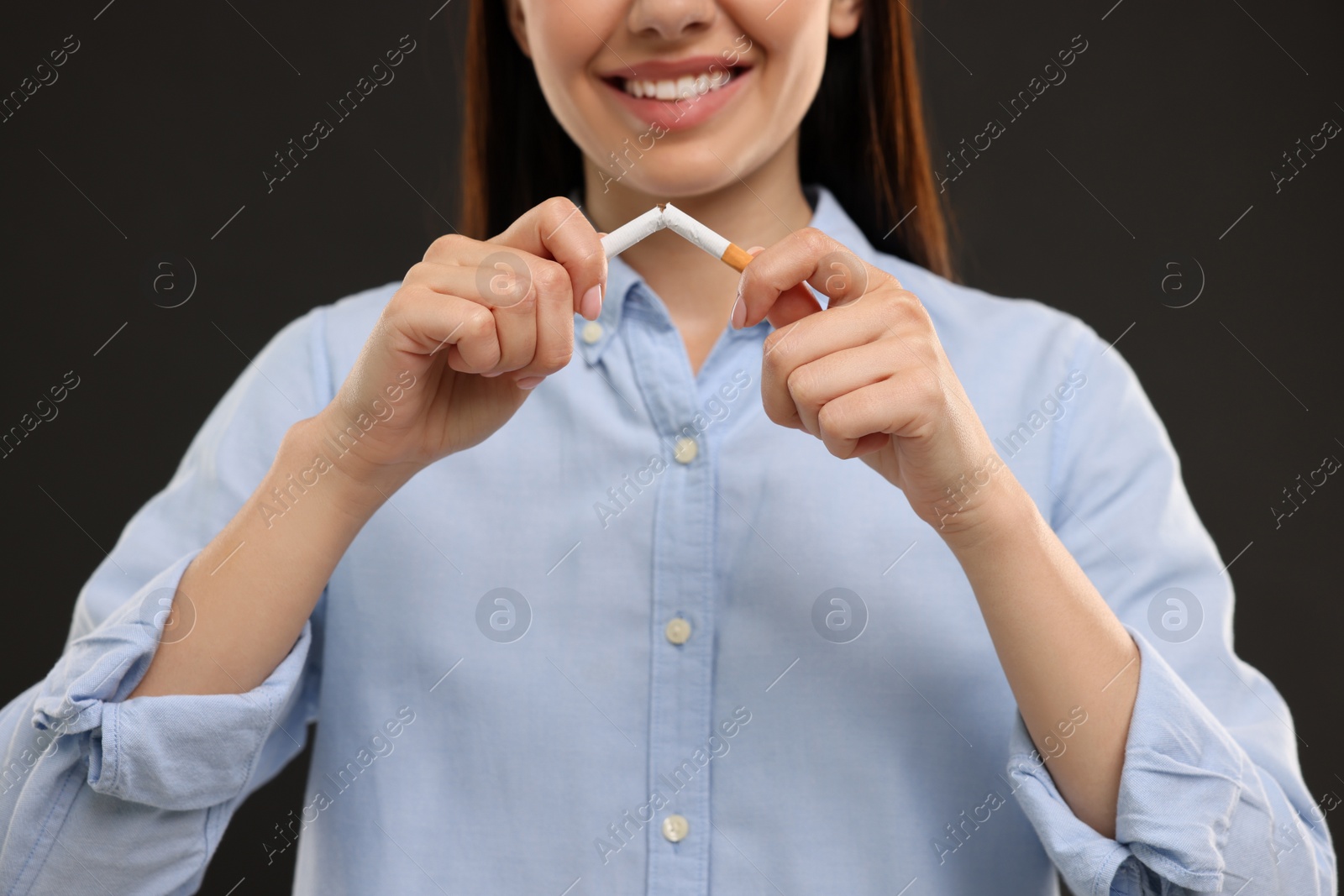 Photo of Stop smoking concept. Happy woman breaking cigarette on black background, closeup