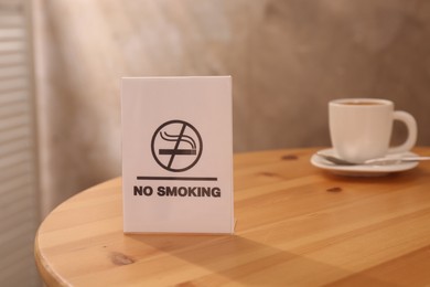 Photo of No Smoking sign and cup of drink on wooden table indoors, selective focus