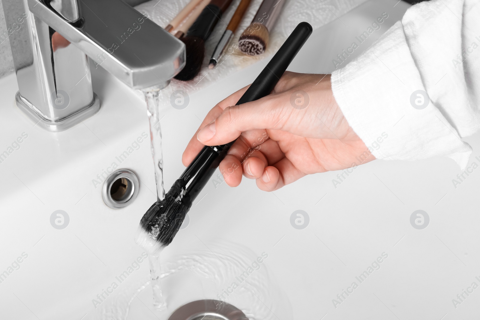 Photo of Woman washing makeup brush under stream of water in sink, closeup