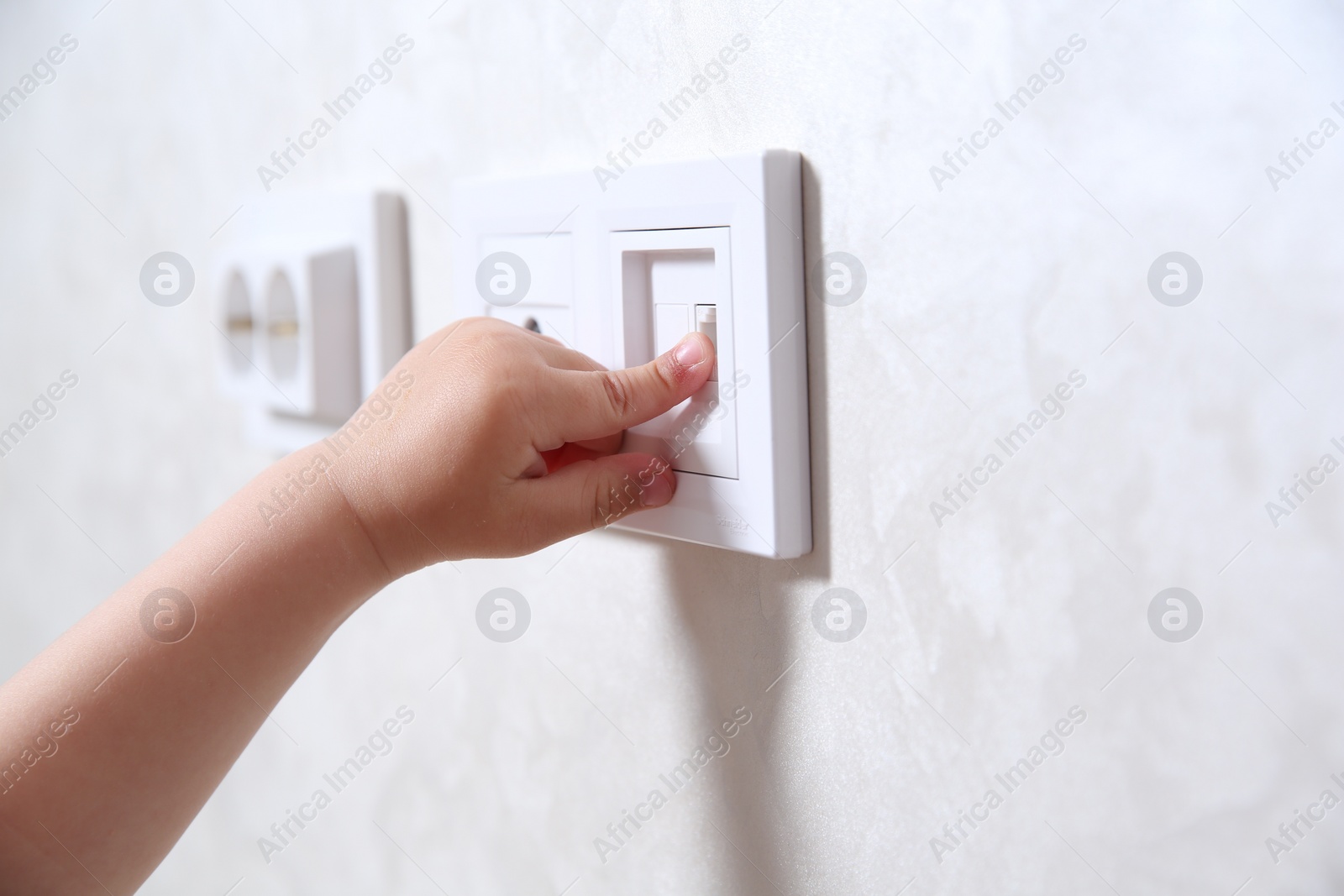 Photo of Little child playing with electrical socket indoors, closeup. Dangerous situation