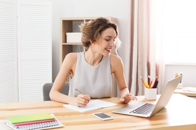 Photo of Young woman working with laptop at desk. Home office