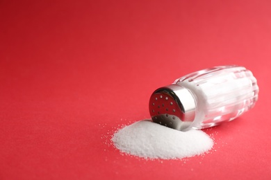 Photo of Scattered salt and shaker on red background, closeup. Space for text