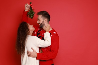 Lovely couple under mistletoe bunch on red background. Space for text