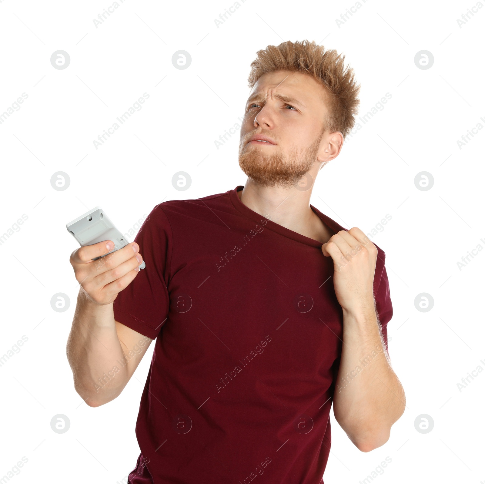 Photo of Young man with air conditioner remote suffering from heat on white background