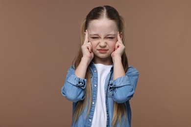 Photo of Little girl suffering from headache on brown background