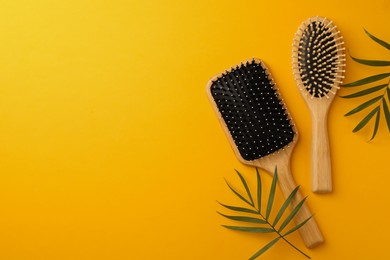 Photo of Wooden hairbrushes and green leaves on orange background, flat lay. Space for text
