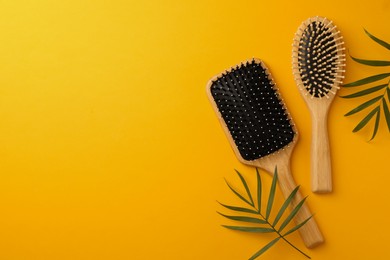 Wooden hairbrushes and green leaves on orange background, flat lay. Space for text