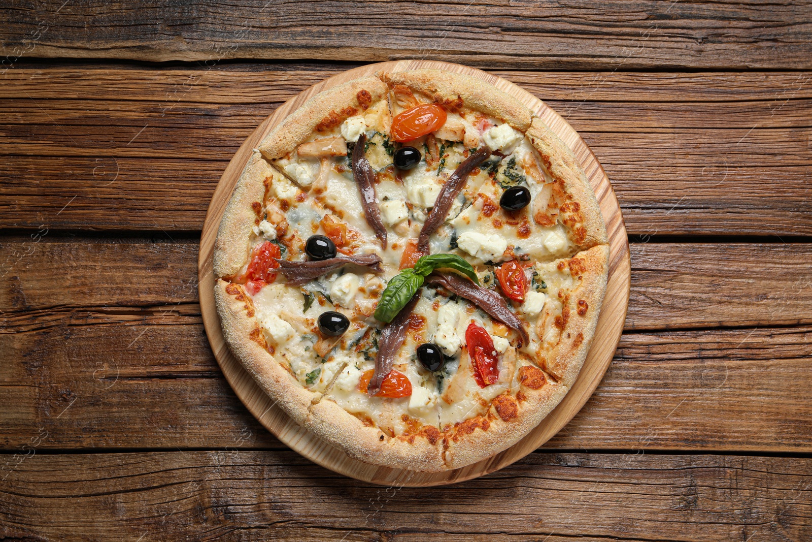Photo of Tasty pizza with anchovies, basil and olives on wooden table, top view
