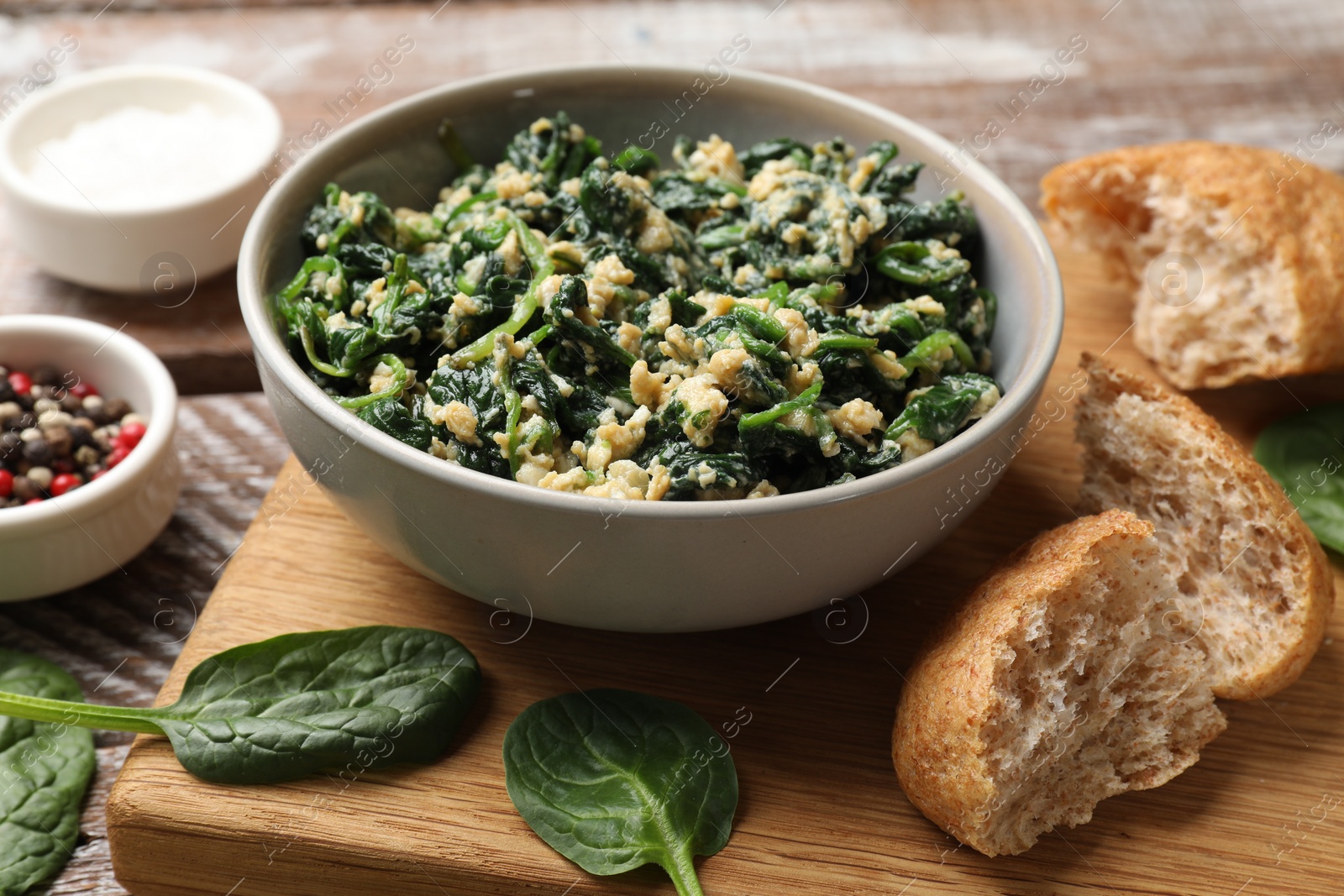 Photo of Tasty spinach dip with egg in bowl, bread and spices on wooden table, closeup