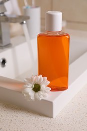 Photo of Fresh mouthwash in bottle and chamomile on sink in bathroom, closeup