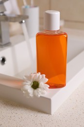 Fresh mouthwash in bottle and chamomile on sink in bathroom, closeup