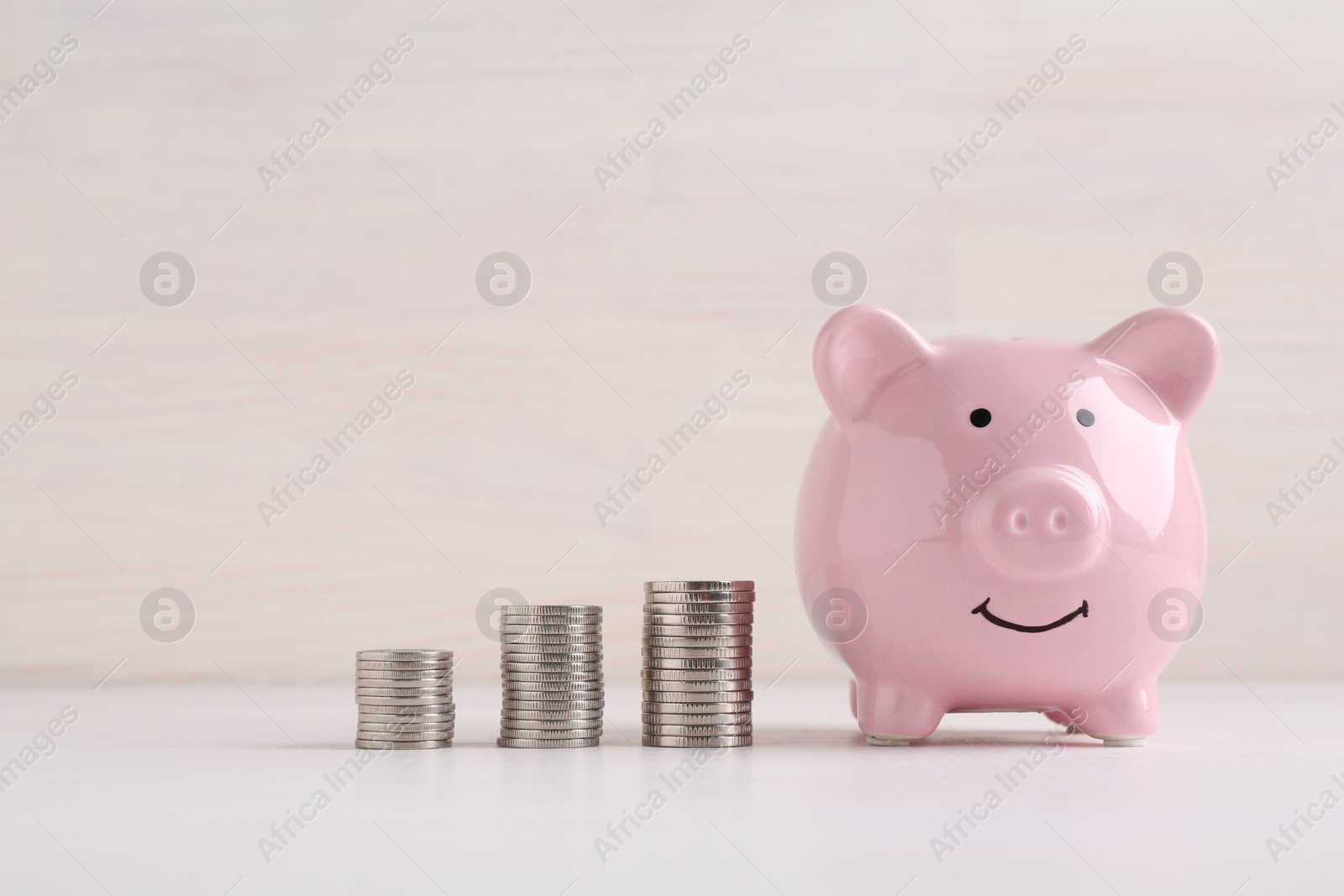 Photo of Financial savings. Piggy bank and stacked coins on white wooden table