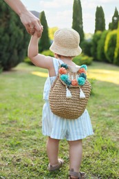 Photo of Cute little girl in stylish clothes holding mother's hand outdoors on sunny day, back view
