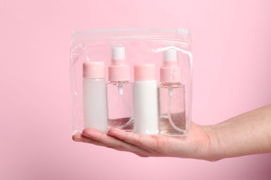 Photo of Cosmetic travel kit. Woman holding plastic bag with small bottles of personal care products against pink background, closeup