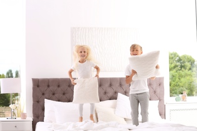 Happy children with pillows jumping on bed at home