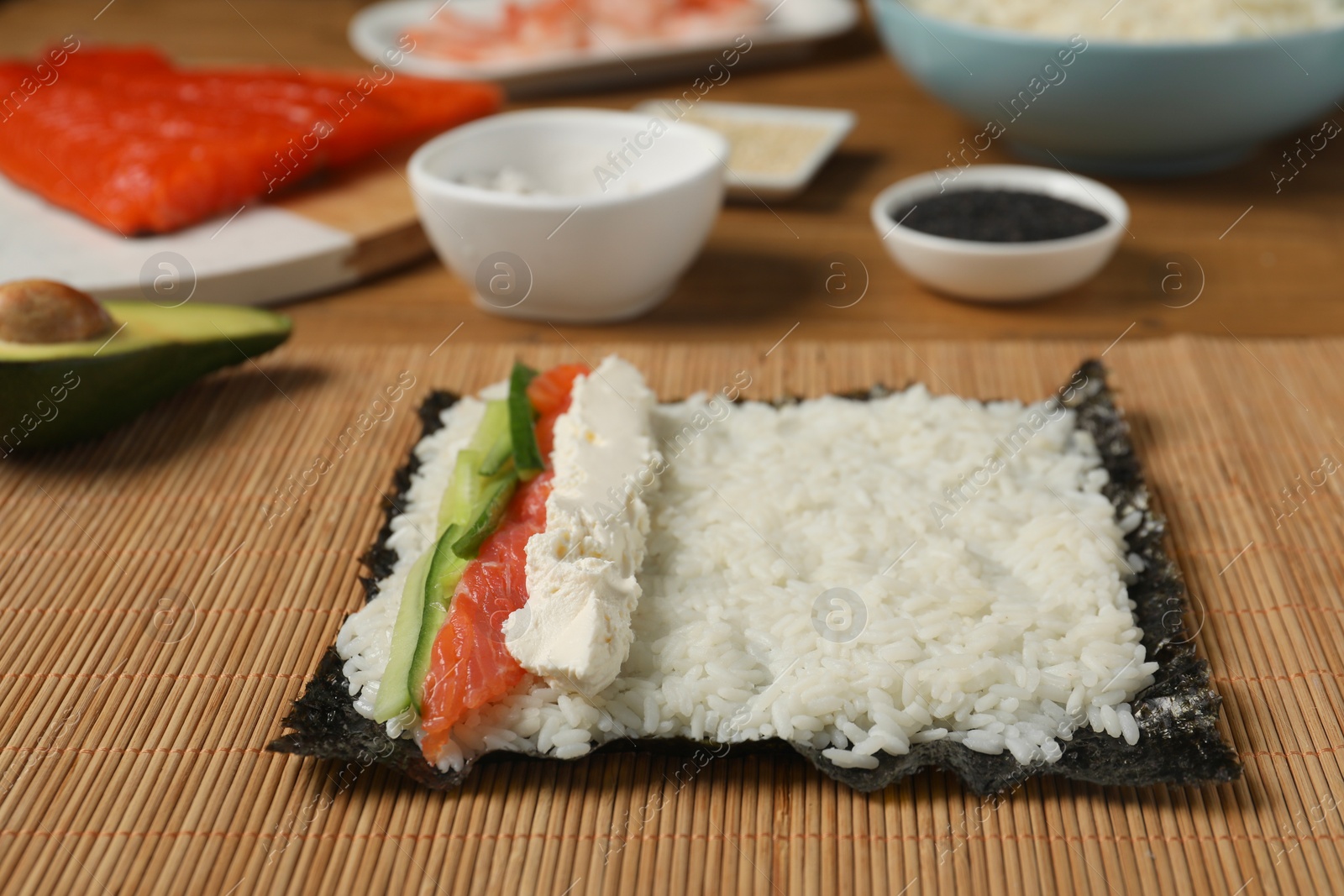Photo of Unwrapped sushi roll with rice, cucumber, cheese and salmon on bamboo mat, closeup