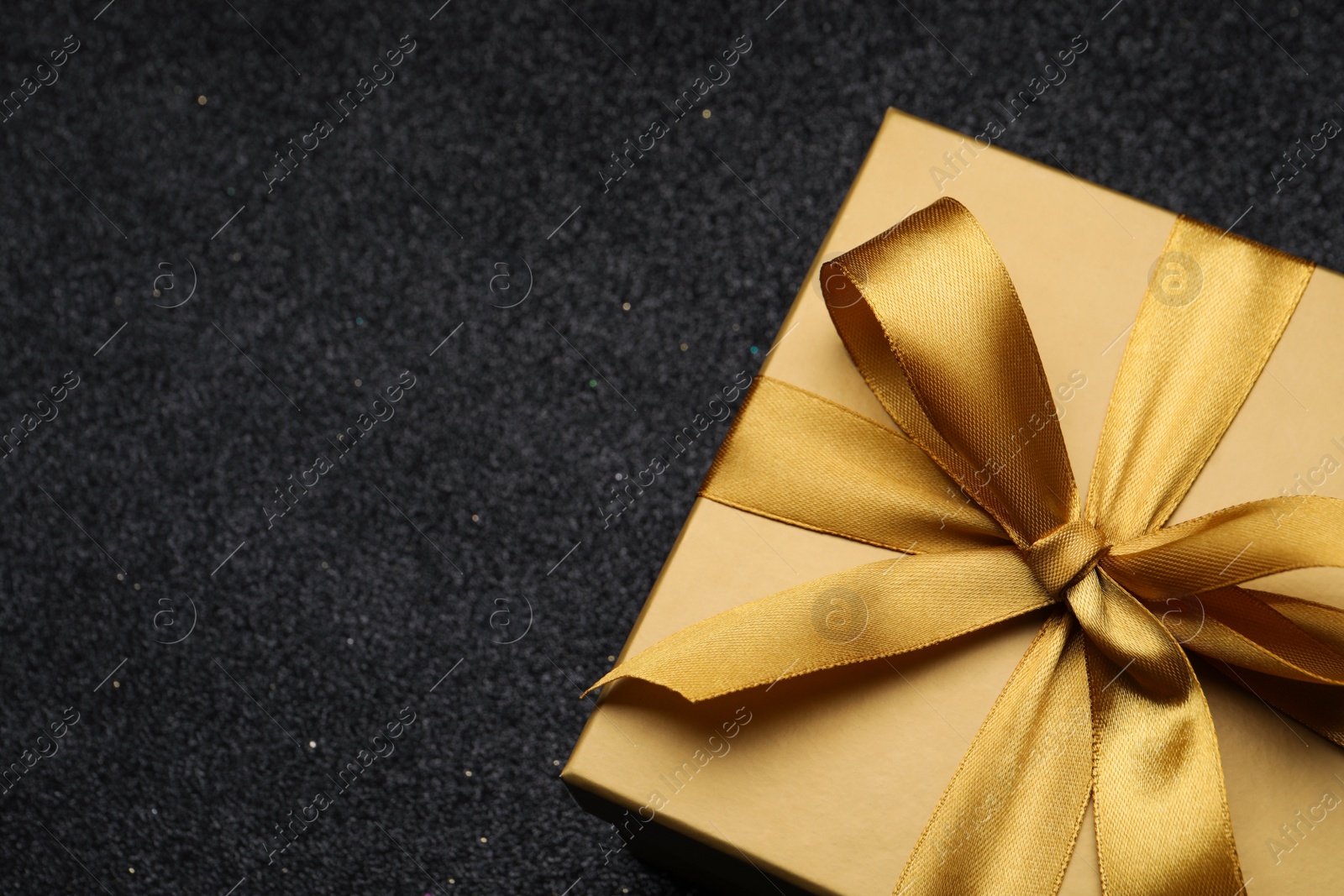 Photo of Golden gift box with satin bow on black background. closeup. Space for text