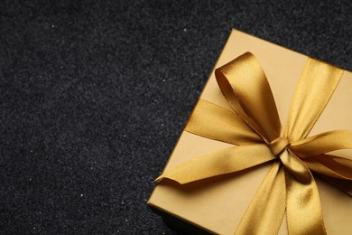 Golden gift box with satin bow on black background. closeup. Space for text