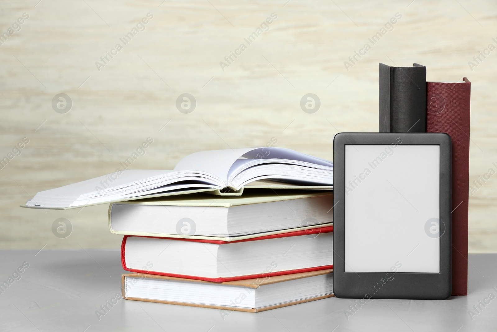 Photo of Portable e-book reader and many hardcover books on white textured table