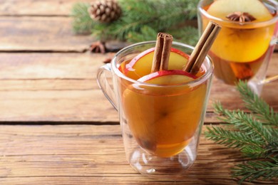 Photo of Hot mulled cider and fir branches on wooden table, space for text
