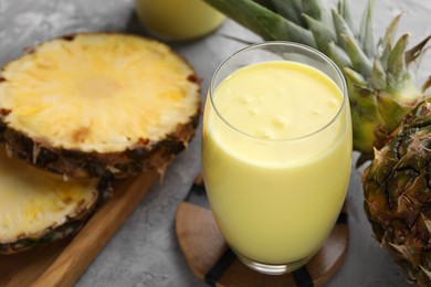 Photo of Tasty pineapple smoothie and fruit on grey table, closeup