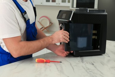 Photo of Repairman fixing coffee machine at table indoors, closeup