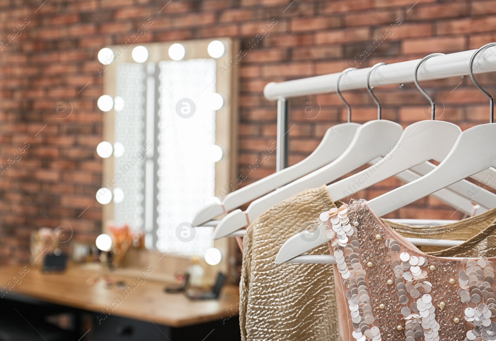 Photo of Hangers with stylish clothes on rack in makeup room