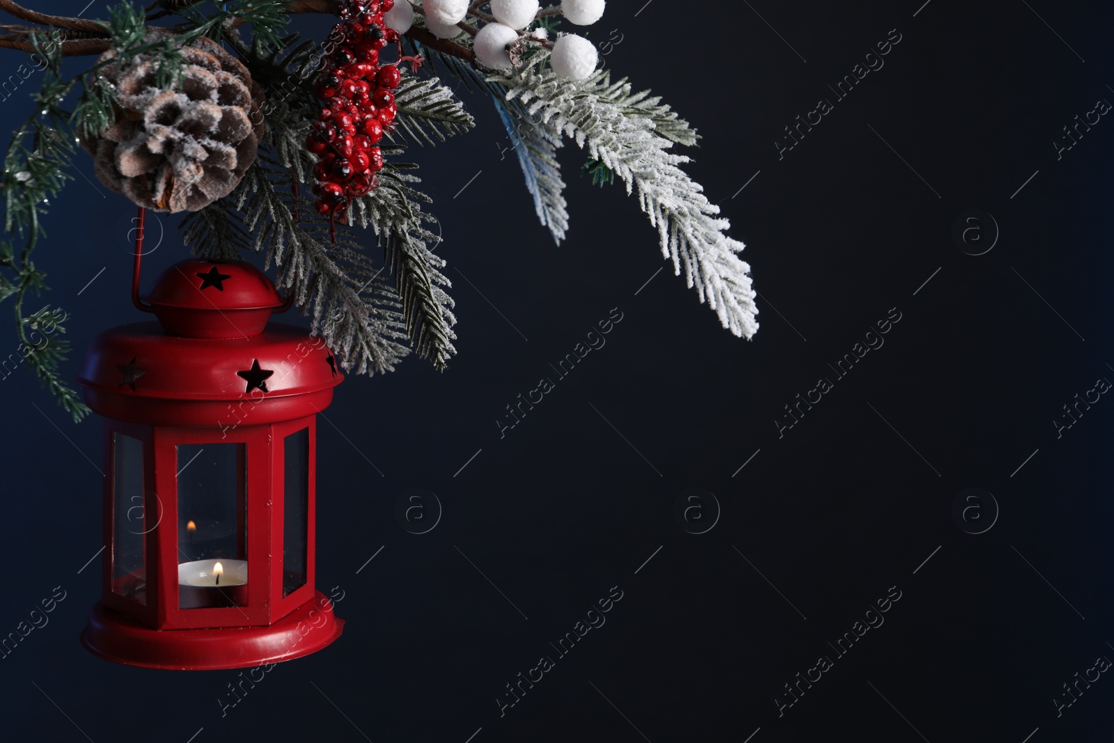 Photo of Christmas lantern with burning candle on fir tree against dark background, closeup. Space for text