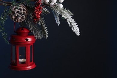 Christmas lantern with burning candle on fir tree against dark background, closeup. Space for text