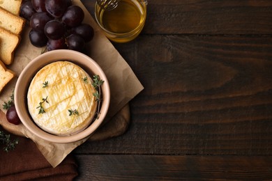 Photo of Tasty baked camembert in bowl, grapes honey and croutons on wooden table, flat lay. Space for text