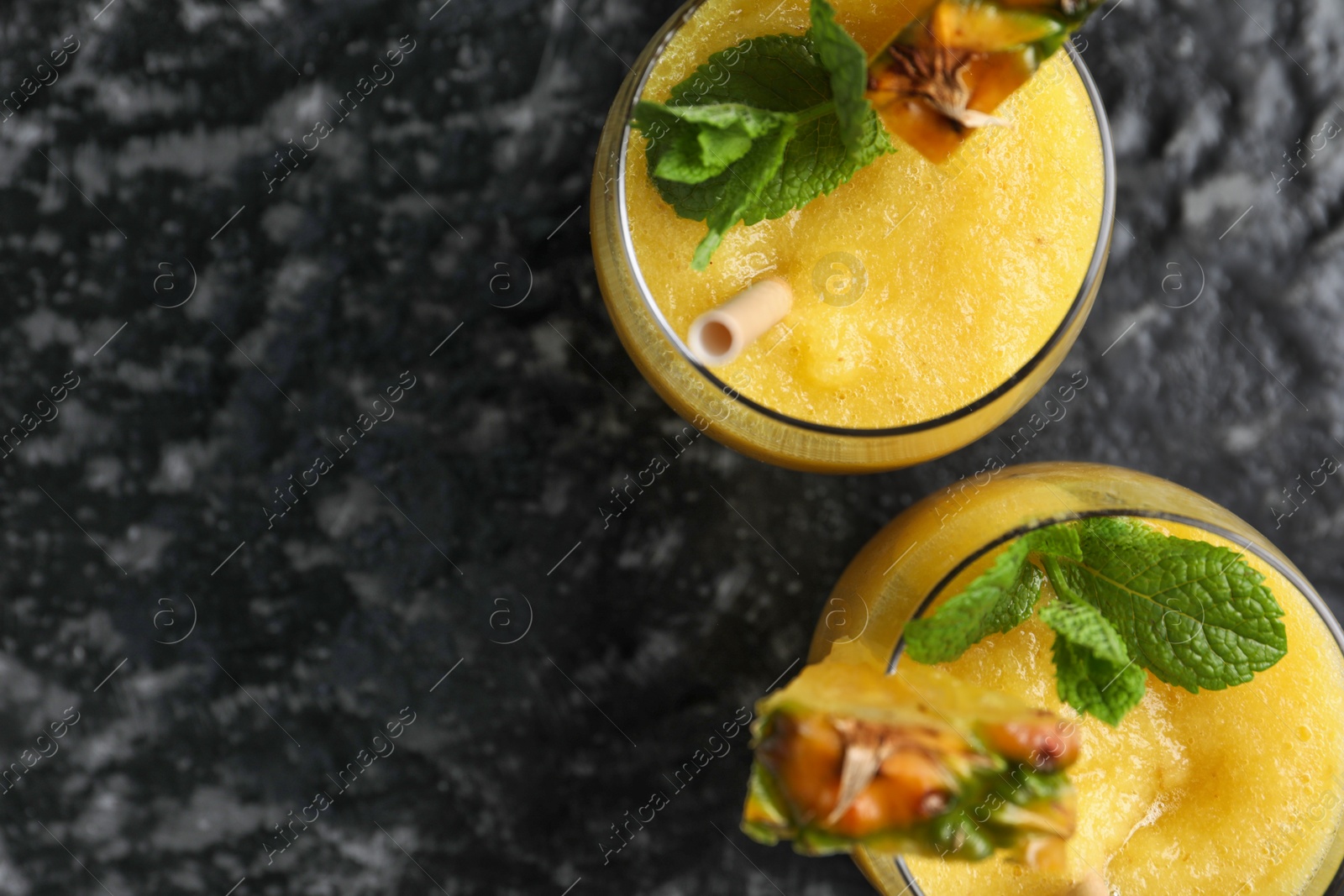 Photo of Tasty pineapple smoothie in glasses on black textured table, top view. Space for text