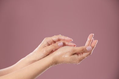 Young woman applying natural scrub on hands against color background