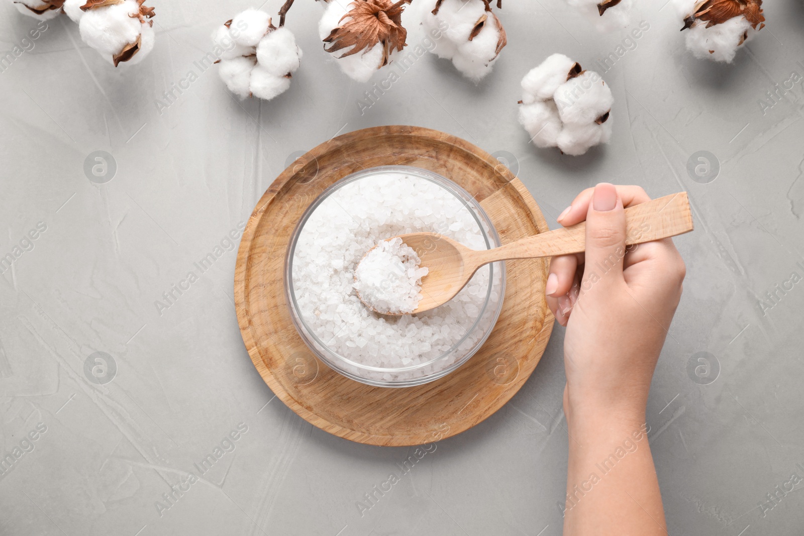 Photo of Woman with white sea salt for spa scrubbing procedure at grey stone table, top view