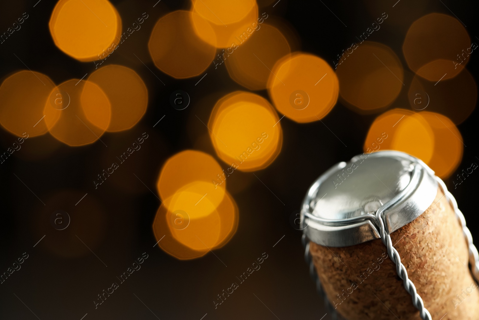 Photo of Sparkling wine cork with muselet cap against blurred festive lights, closeup. Space for text