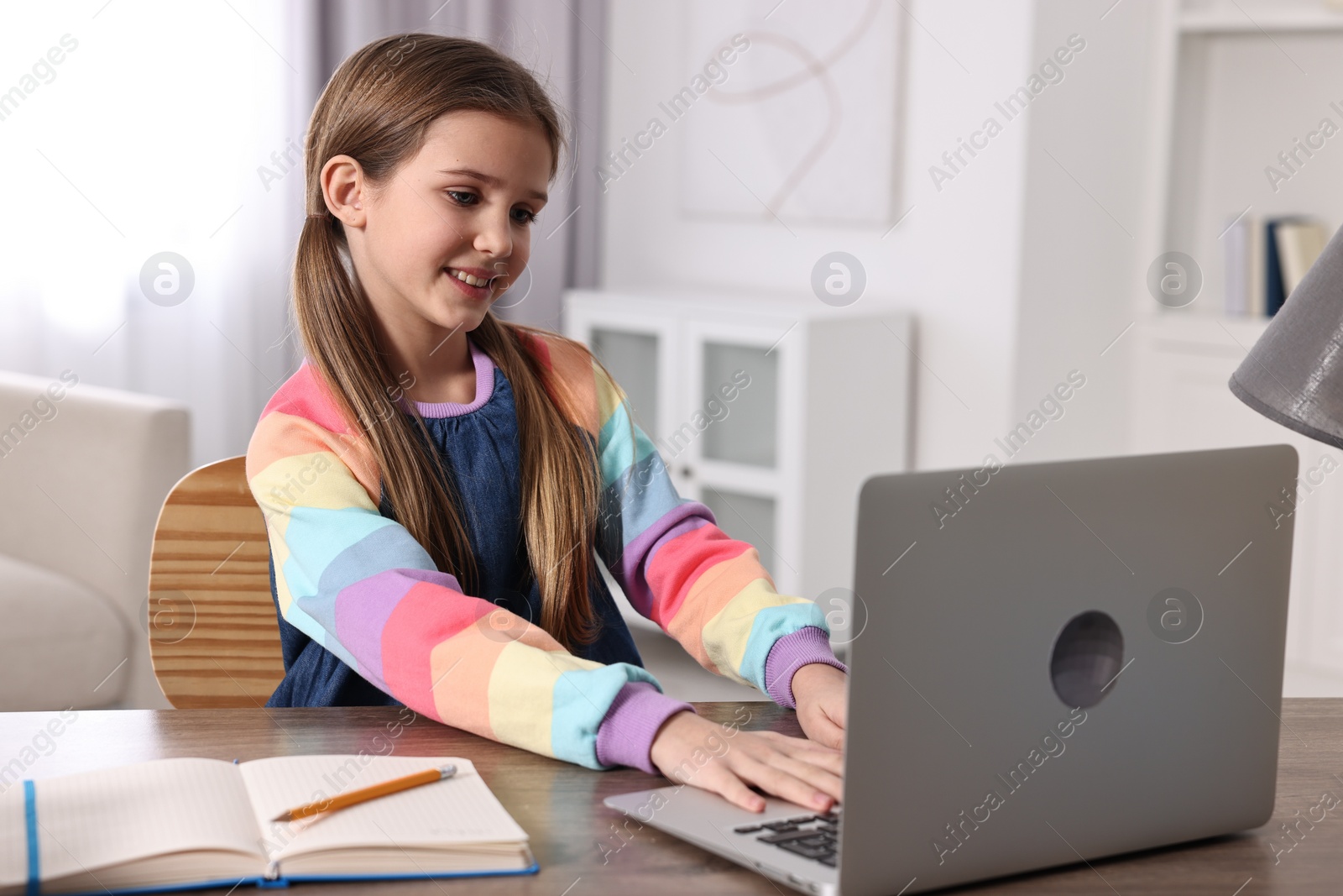 Photo of E-learning. Cute girl using laptop during online lesson at table indoors