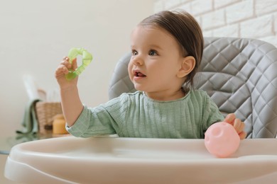 Cute little baby with teether and toy in high chair indoors