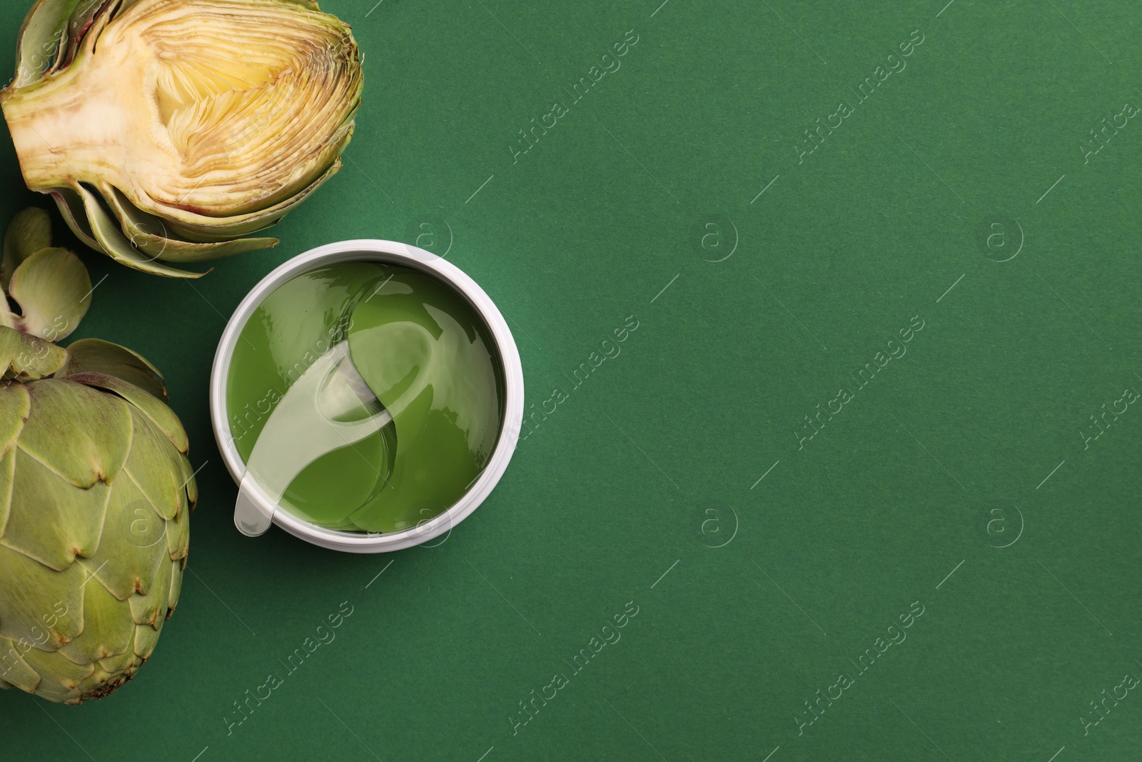 Photo of Package of under eye patches and artichokes on green background, flat lay with space for text. Cosmetic product