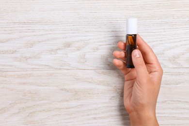 Woman with bottle of essential oil on wooden background, closeup. Space for text