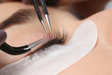 Photo of Young woman undergoing eyelashes extensions procedure, closeup