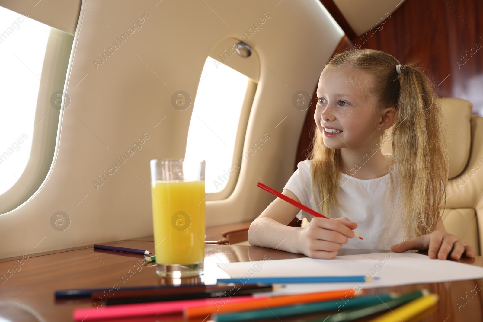 Photo of Cute little girl drawing at table in airplane during flight