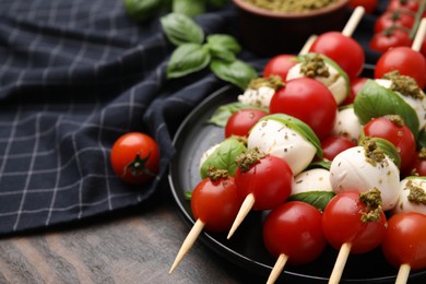 Caprese skewers with tomatoes, mozzarella balls, basil and pesto sauce on wooden table, closeup. Space for text